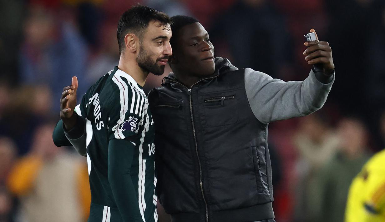 Seorang fans melakukan selfie bareng gelandang Manchester United, Bruno Fernandes setelah berakhirnya laga pekan ke-9 Liga Inggris 2023/2024 antara Sfheffield United menghadapi Manchester United di Bramall Lane, Sheffield, Minggu (22/10/2023) dini hari WIB. (AFP/Darren Staples)