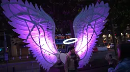 Pengunjung berpose dengan karya seni "Angels of Freedom" dari Israel yang ditampilkan selama festival seni visual tahunan Light Night Leeds di Leeds, utara Inggris, 10 Oktober 2019. Festival tersebut mengambil alih jalanan pusat kota Leeds selama dua malam di bulan Oktober. (Oli SCARFF/AFP)