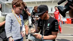 Pebalap Mercedes, Lewis Hamilton memberikan tanda tangan kepada seorang anak di area paddock Sirkuit Autodromo Hermanos Rodriguez, Mexico City, Meksiko, (29/10/2015). (AFP Photo/Alfredo Estrella)