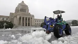 Seorang pria menggunakan alat berat untuk membersihkan salju di halaman Gedung Diet di Tokyo, Jepang, Senin (18/1). Akibat banyaknya tumpukan salju yang menyelimuti daerah metropolitan Tokyo, moda transportasi massa pun lumpuh. (AFP/JIJI Press Japan Out)