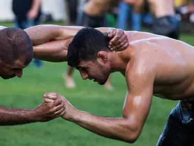Dua pegulat sedang beraksi berusaha saling menjatuhkan dalam kompetisi tahunan gulat minyak tradisional di Sochos, Yunani, 30 Juni 2018. Lebih dari seratus drum minyak zaitun habis untuk melumuri sekujur tubuh setiap peserta. (AP/Giannis Papanikos)