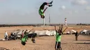 Dua pemuda melompat di udara saat menunjukkan keterampilan parkour mereka di dekat tenda warga di perbatasan Gaza, Palestina (10/4). Mereka menghibur para warga yang melakukan aksi protes di perbatasan Gaza tersebut. (AFP Photo/Said Khatib)