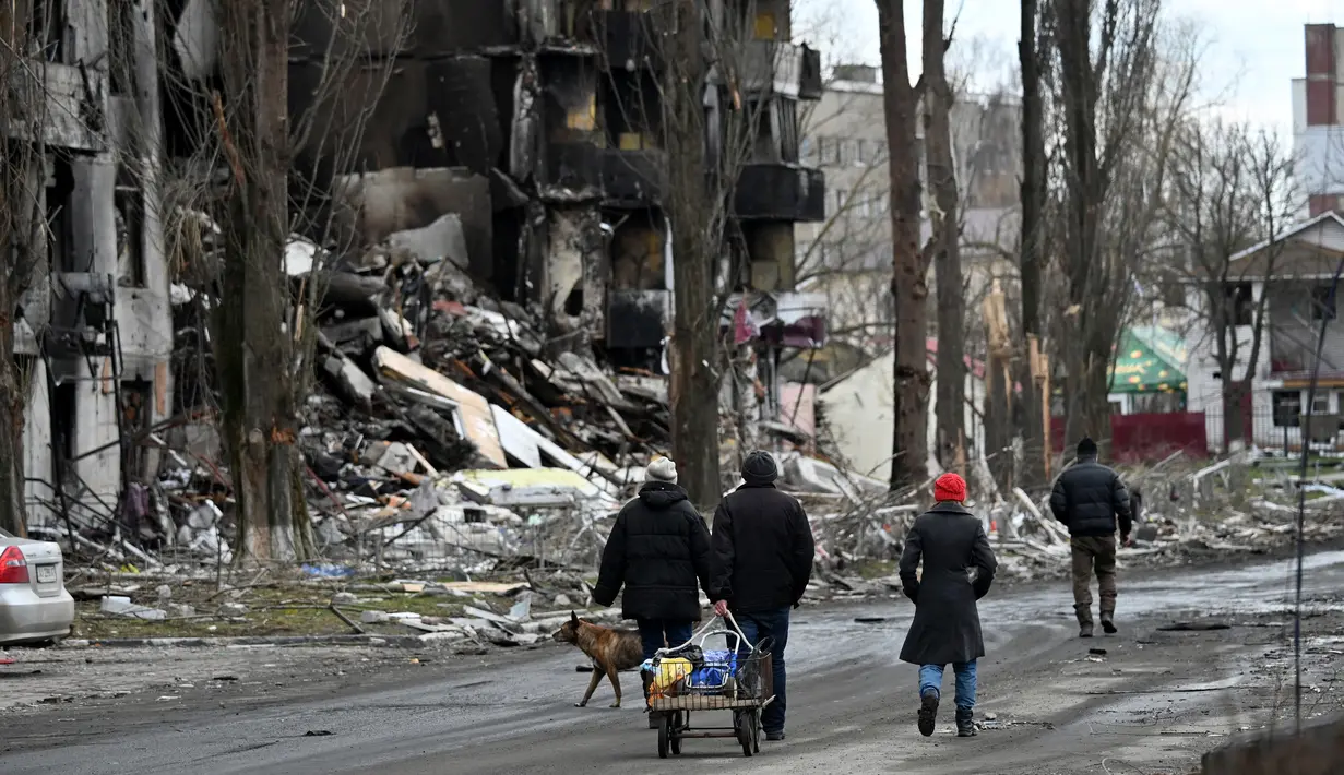 Orang-orang berjalan melewati bangunan yang hancur di kota Borodianka, barat laut Kiev pada 4 April 2022. Saat pasukan Rusia mundur, kota kecil Borodianka, 50 km barat laut Kiev, menjadi reruntuhan. (Sergei SUPINSKY / AFP)