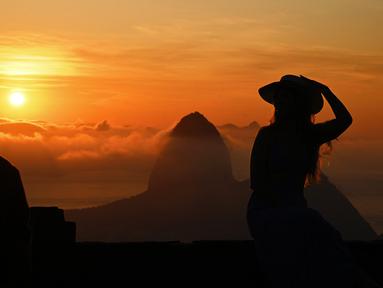 Seorang turis berpose saat matahari terbit dengan latar belakang gunung Sugarloaf di Bukit Corcovado di Rio de Janeiro, Brasil, pada 24 Maret 2023. Lokasi gunung Corcovado yang cukup tinggi juga menarik wisatawan untuk bisa menyaksikan kota Rio de Janeiro dari puncaknya. (Photo by Carl DE SOUZA / AFP)