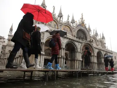 Sejumlah warga berjalan melewati papan saat gelombang pasang membuat banjir depan Basilika Santo Markus, Venesia, Italia, Selasa (12/11/2019). Venesia dilanda banjir akibat gelombang pasang setinggi 127 cm. (AP Photo/Luca Bruno)