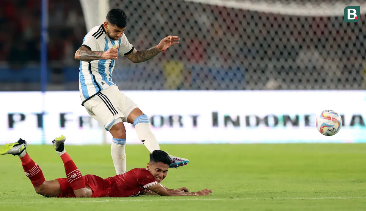 Pemain Timnas Indonesia, Marselino Ferdinan (bawah) terjatuh ketika berebut dengan pemain Argentina, Cristian Romero pada laga FIFA Matchday di Stadion Utama Gelora Bung Karno (SUGBK), Senayan, Jakarta, Senin (19/06/2023). (Bola.com/Bagaskara Lazuardi)
