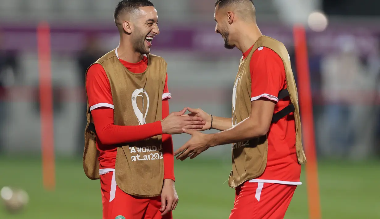 Gelandang Maroko, Hakim Ziyech berbicara reken setimnya Selim Amallah selama sesi latihan di Stadion Al Duhail SC di Doha (16/12/2022). Maroko akan bertanding melawan Kroasia untuk memperebutkan juara 3 Piala Dunia 2022. Keduanya dipertemukan kembali setelah pernah bertanding pada babak penyisihan grup F lalu. (AFP/Karim Jafaar)