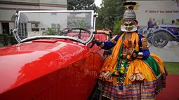 Penari berpose dengan mobil vintage yang baru direstorasi dalam pameran 21 Gun Salute Heritage and Cultural Trust di New Delhi, India, Selasa (6/2). (AP Photo/Altaf Qadri)