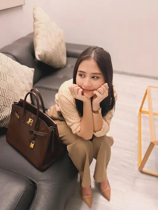 Potret lain memperlihatkan Prilly tampil chic dengan padu padan striped long shirt warna brick, loose pants warna beige, dan tas Hermes Birkin B35 bordeaux togo leather with gold hardware seharga Rp329 jutaan. [@prillylatuconsina96]