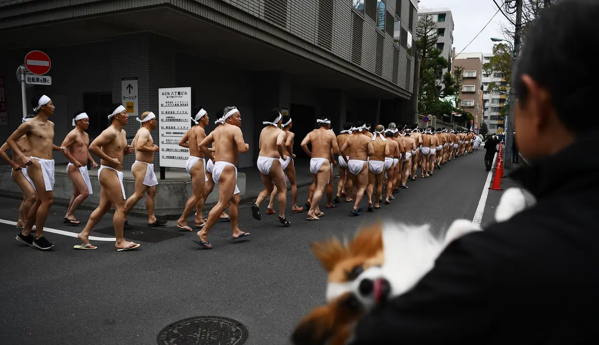 Orang-orang percaya Shinto dari Kuil Teppozu Inari berlarian di sekitar kuil untuk menghangatkan diri sebelum mandi di air dingin untuk memurnikan jiwa dan tubuh mereka selama ritual Tahun Baru di Tokyo (12/1/2020).  (AFP/Charly Triballeau)