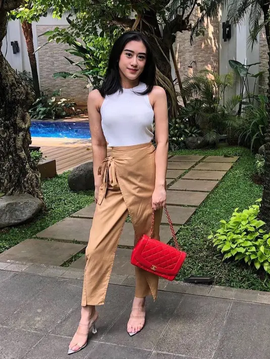 Kusuma Puteri tampil santai dengan atasan tank top putih dipadukan celana coklat dengan apron. Ia juga membawa tas merah dari Chanel. [@kusumaputeri]