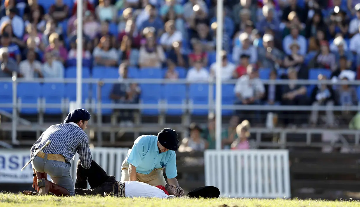 Petugas membantu seorang gaucho yang terjatuh saat menunggangi kuda liar dalam perayaan Pekan Creole di Montevideo, Uruguay, Para gaucho ini akan memperebutkan gelar pengendara terbaik. (REUTERS/Andres Stapff)