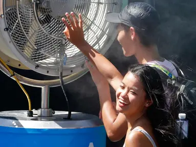 Penonton berdiri di depan kipas pendingin saat menyaksikan pertandingan turnamen tenis Australia Terbuka 2018 di Melbourne, Australia, (16/1). Teriknya matahari membuat peserta dan penonton kepanasan. (AP Photo / Ng Han Guan)