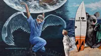 Seorang wanita memandangi mural yang menggambarkan petugas kesehatan dengan sayap memegang bola dunia pada Hari Perawat Internasional di Melbourne,Australia, Selasa (12/5/2020). Petugas medis menghadapi risiko besar di tengah pandemi virus corona COVID-19 seperti sekarang ini. (William WEST/AFP)