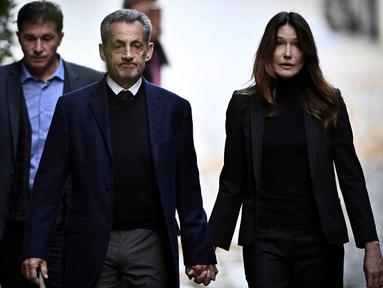 Mantan Presiden Prancis Nicolas Sarkozy (tengah), bersama istrinya Carla Bruni-Sarkozy, berjalan meninggalkan kediamannya untuk menyerahkan diri ke Penjara La Sante guna menjalani hukuman penjara lima tahun setelah dinyatakan bersalah atas konspirasi kriminal terkait rencana pendanaan kampanye pemilu 2007-nya oleh diktator Libya Moamer Kadhafi, di Paris, pada 21 Oktober 2025. (JULIEN DE ROSA/AFP)