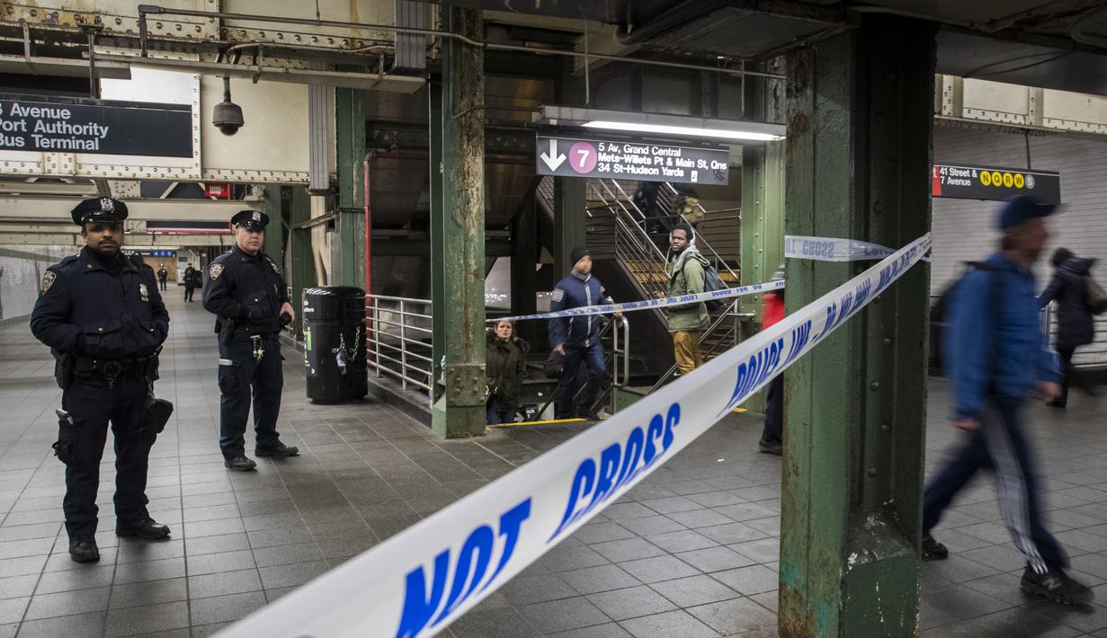 Penumpang melintasi aparat kepolisian yang berjaga di lorong stasiun kereta bawah tanah dekat lokasi teror bom pipa di New York City, Senin (11/12). Empat orang dikabarkan mengalami luka-luka akibat teror bom tersebut. (Drew Angerer/Getty Images/AFP)