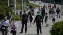 Petugas berpatroli ketika keluarga dengan anak-anak berjalan di Barcelona, Spanyol (26/4/2020). Pemerintah Spanyol akhirnya tunduk pada tekanan publik yang menginginkan kebebasan anak-anak berusia di bawah 14 tahun untuk keluar rumah dengan pengawasan orang tua . (AP/Emilio Morenatti)