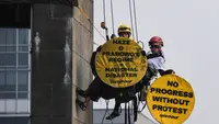 Aktivis Greenpeace Indonesia bergelantungan di Patung Selamat Datang sambil membentangkan poster berisi pesan protes di kawasan Bundaran Hotel Indonesia, Jakarta, Selasa (20/10/2026). Aksi tersebut digelar bertepatan dengan dua tahun pelantikan Presiden Prabowo Subianto. Para aktivis mendesak pemerintah mengambil langkah untuk mengatasi krisis iklim yang kian memburuk dan kenaikan biaya hidup. (BAY ISMOYO/AFP)