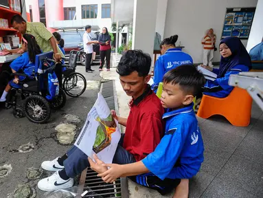 Aktivitas siswa penyandang disabilitas membaca buku pada perpustakaan keliling Sudin perpustakaan Jakarta Selatan di halaman Sekolah YPAC, jakarta, Jumat (29/11/2024). (merdeka.com/Arie Basuki)
