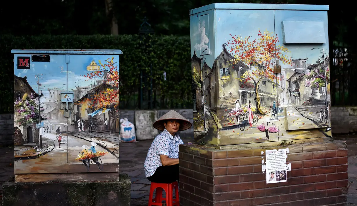 Pedagang menunggu pelanggan sambil duduk di belakang kotak listrik yang dihiasi lukisan di Hanoi, ibu kota Vietnam pada 11 Agustus 2020. Setelah mencatat nol kasus COVID-19 selama lebih dari tiga bulan, Vietnam melaporkan sejumlah infeksi baru di dalam negeri sejak akhir Juli. (MANAN VATSYAYANA/AFP)