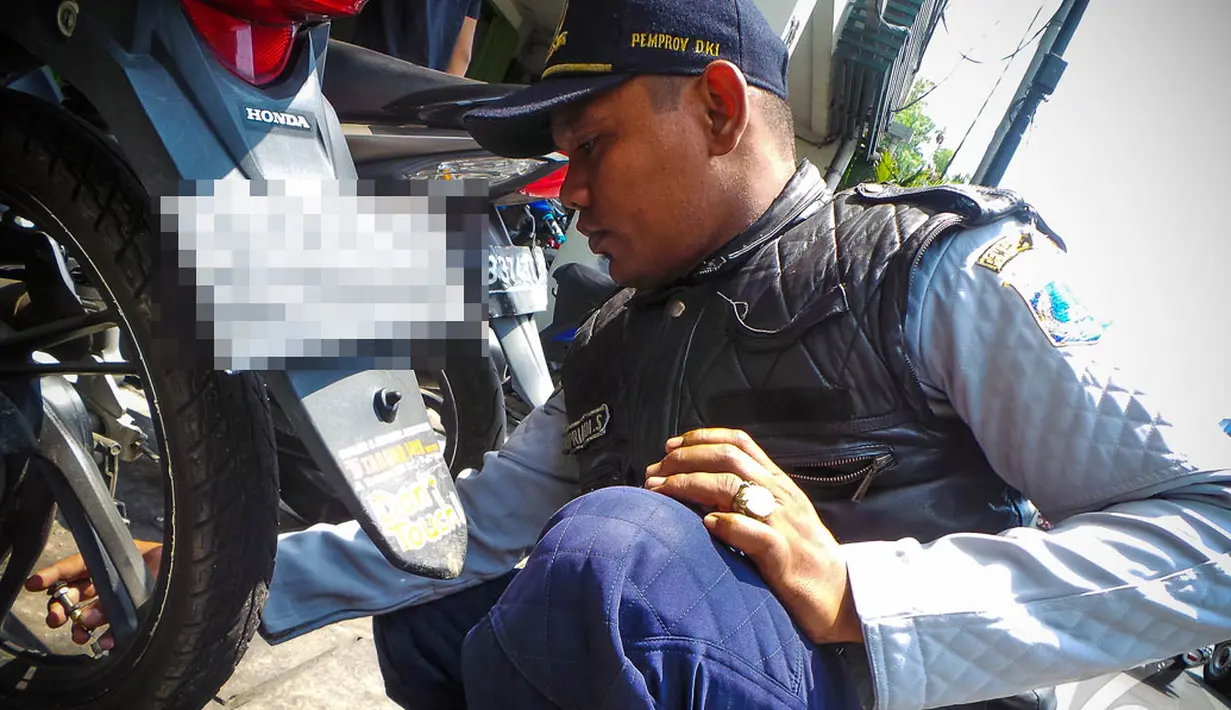 Seorang petugas mencabut pentil sebuah sepeda motor yang parkir liar di kawasan Glodok Jakarta, Selasa (9/9/2014) (Liputan6.com/Faizal Fanani)