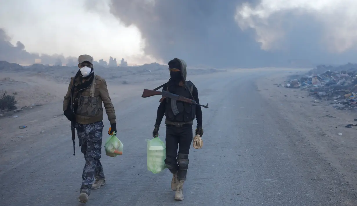 Petugas kepolisian berjalan di dekat kilang minyak yang dibakar oleh ISIS di Qayyara, selatan Mosul, Irak, (23/11). Sebelumnya, sekitar enam sumur minyak telah dibakar ISIS di kawasan tersebut. (REUTERS/Goran Tomasevic)