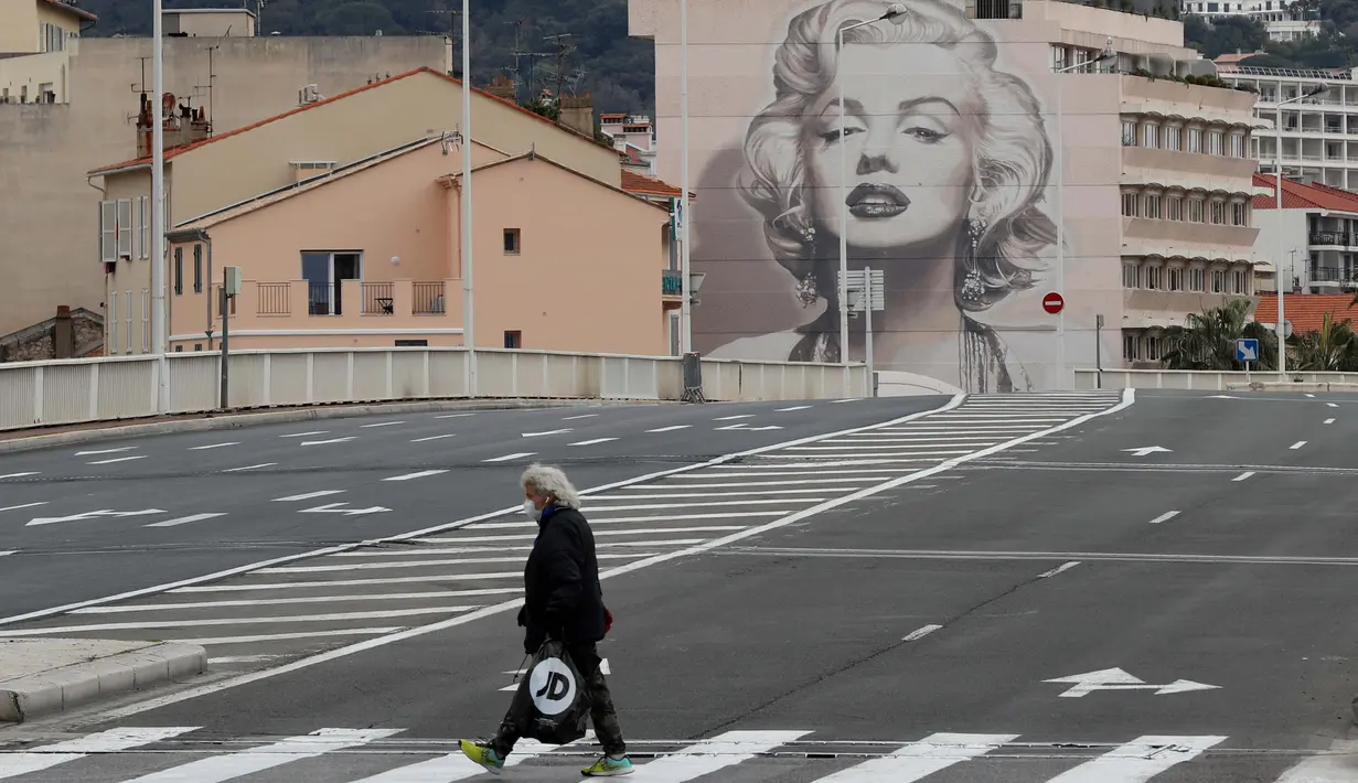 Seorang pria yang mengenakan masker melintasi jalan saat Prancis memberlakukan lockdown untuk menghentikan penyebaran pandemi virus corona Covid-19 di Cannes pada 23 Maret 2020. (Photo by VALERY HACHE / AFP)