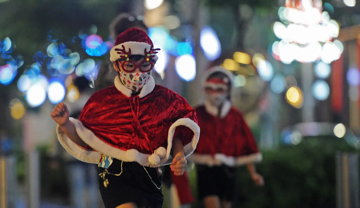 Seorang gadis kecil mengenakan kostum Sinterklas menikmati pemandangan dekorasi lampu Natal di tengah hujan rintik di sepanjang pusat perbelanjaan Orchard Road di Singapura (16/12/2020). Presiden Halimah Yacob telah menekan tombol sebagai tanda menyambut Natal 2020. (Xinhua/Then Chih Wey)