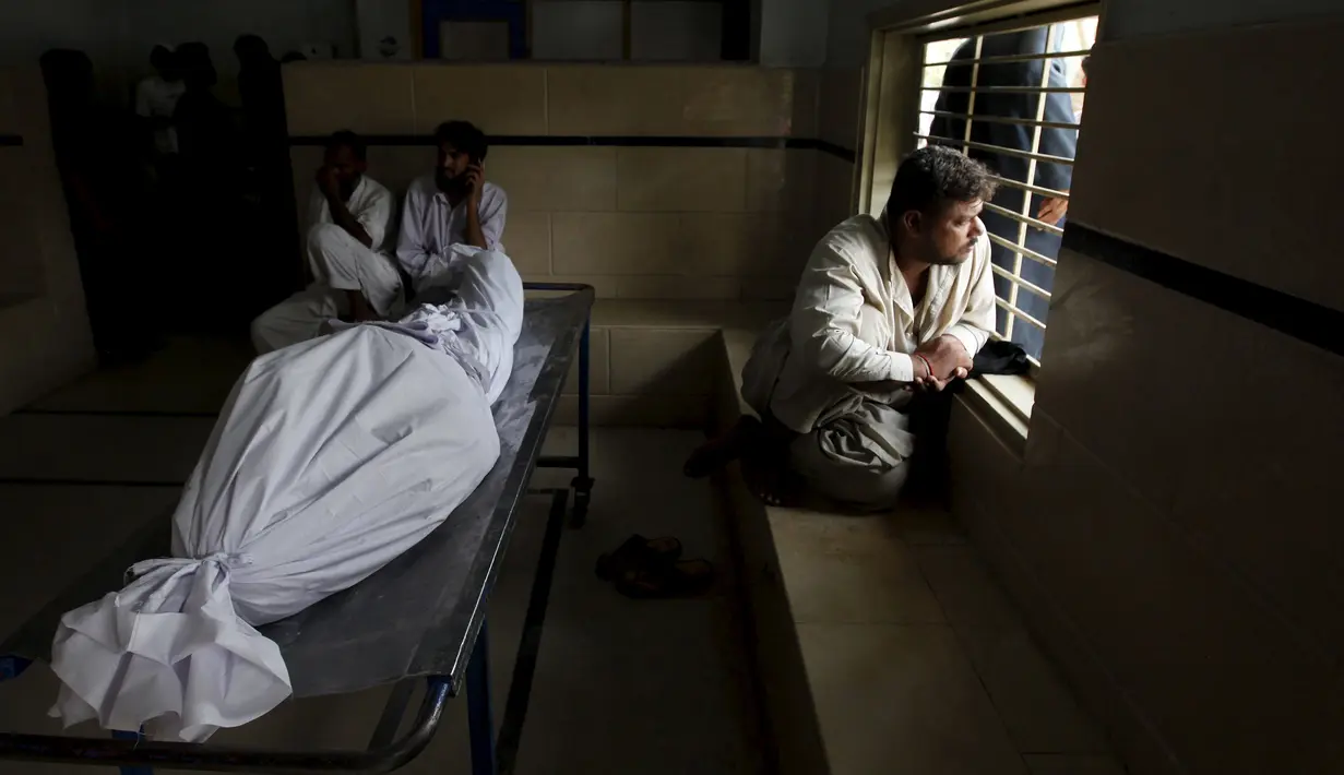 Seorang kerabat duduk dekat jenazah korban gelombang panas sambil menungggu ambulans, di sebuah kamar mayat di Karachi, Pakistan, Senin (22/6). Fenomena gelombang panas yang mendera Pakistan telah menewaskan setidaknya 120 orang. (REUTERS/Akhtar Soomro)
