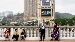 Wisatawan bersantai di sebuah jembatan dengan latar belakang resor kasino The Venetian di Macau, 5 Maret 2019. Macau masuk dalam daerah administrasi khusus di daratan China. (Anthony Wallace/AFP)
