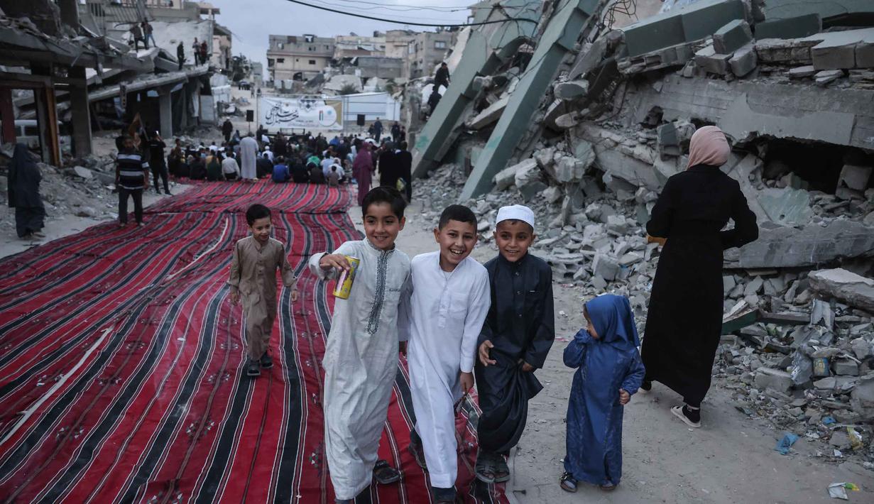 Para pemuda Palestina tertawa bersama saat para jemaah berkumpul di jalan yang rusak parah untuk melaksanakan salat menandai dimulainya Idul Adha, Hari Raya Kurban, di Khan Yunis, Jalur Gaza Selatan, pada Rabu 27 Mei 2026. (BASHAR TALEB/AFP)