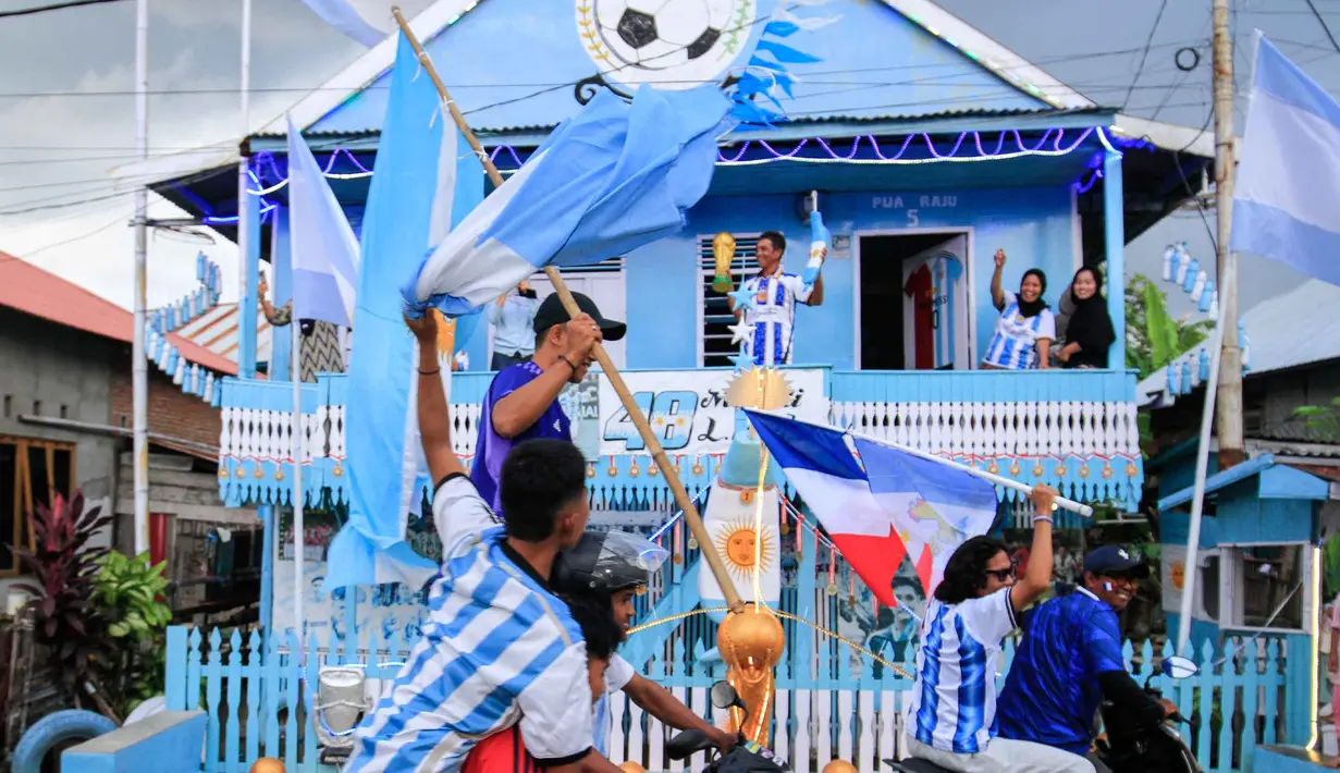 Penggemar Timnas Argentina yang juga seorang nelayan, Muhammad Yusuf (belakang tengah) memegang replika trofi Piala Dunia saat penggemar sepak bola melewati rumahnya dalam konvoi menyambut turnamen sepak bola Piala Dunia 2026 di Polewali Mandar, Sulawesi Barat, Kamis 11 Juni 2026. (Muhammad SALIM/AFP)