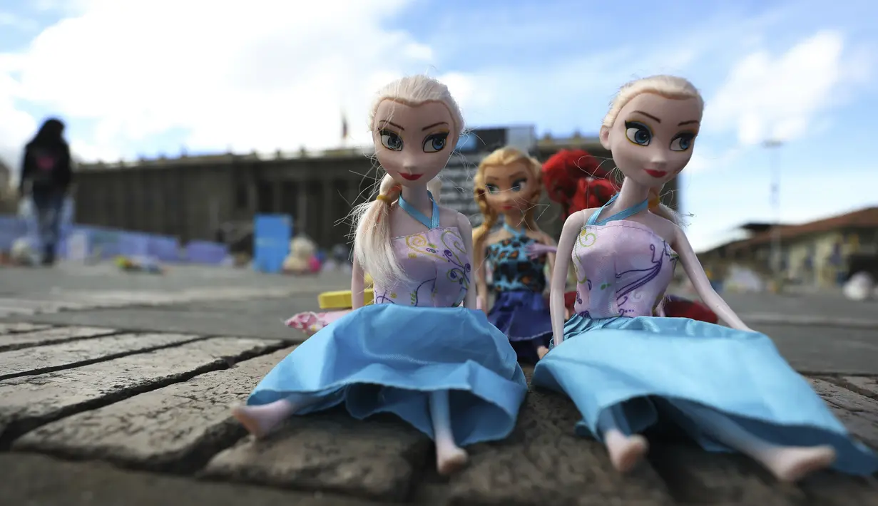 Seorang perempuan melewati boneka yang mewakili anak korban kekerasan selama protes di alun-alun Bolivar di Bogota, Kolombia, Senin (30/11/2020). Ratusan mainan, boneka, dan action figure diletakkan di Bolivar Square untuk memprotes kekerasan terhadap anak-anak. (AP Photo/Fernando Vergara)