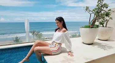 Yuki Kato tampak bahagia saat bermain air di sebuah kolam renang hotel di Bali. Menggunakan pakaian putih dan celana garis-garis warna-warni, latar belakang lautan dan langit biru menambah keindahan pemandangan.(Liputan6.com/IG/@yukikt)