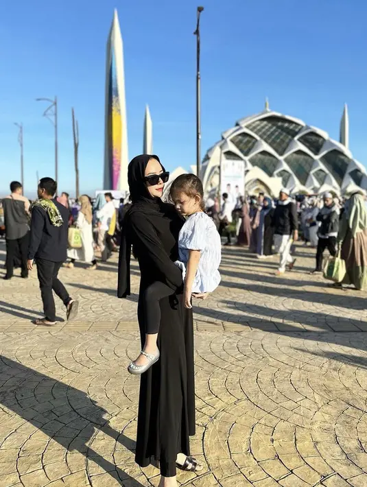 Aura Kasih tampil mengenakan dress hitam serasi dengan pashmina dan sandal Hermesnya saat menggendong putrinya. @aurakasih