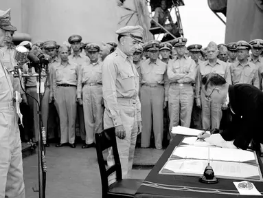 Jenderal AS Douglas MacArthur (kiri) menyaksikan Menteri Luar Negeri Jepang Manoru Shigemitsu menandatangani dokumen penyerahan di atas kapal perang USS Missouri, Teluk Tokyo, 2 September 1945. Penandatanganan ini menandai berakhirnya Perang Dunia II. (AP Photo/C.P. Gorry, File)