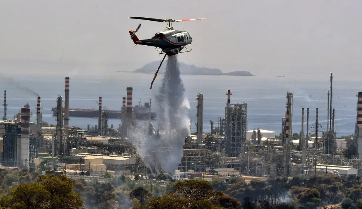<p>Helikopter pemadam kebakaran menyemprotkan air saat terjadi kebakaran hutan dekat kilang minyak di Agioi Theodoroi. (Valerie GACHE/AFP)</p>