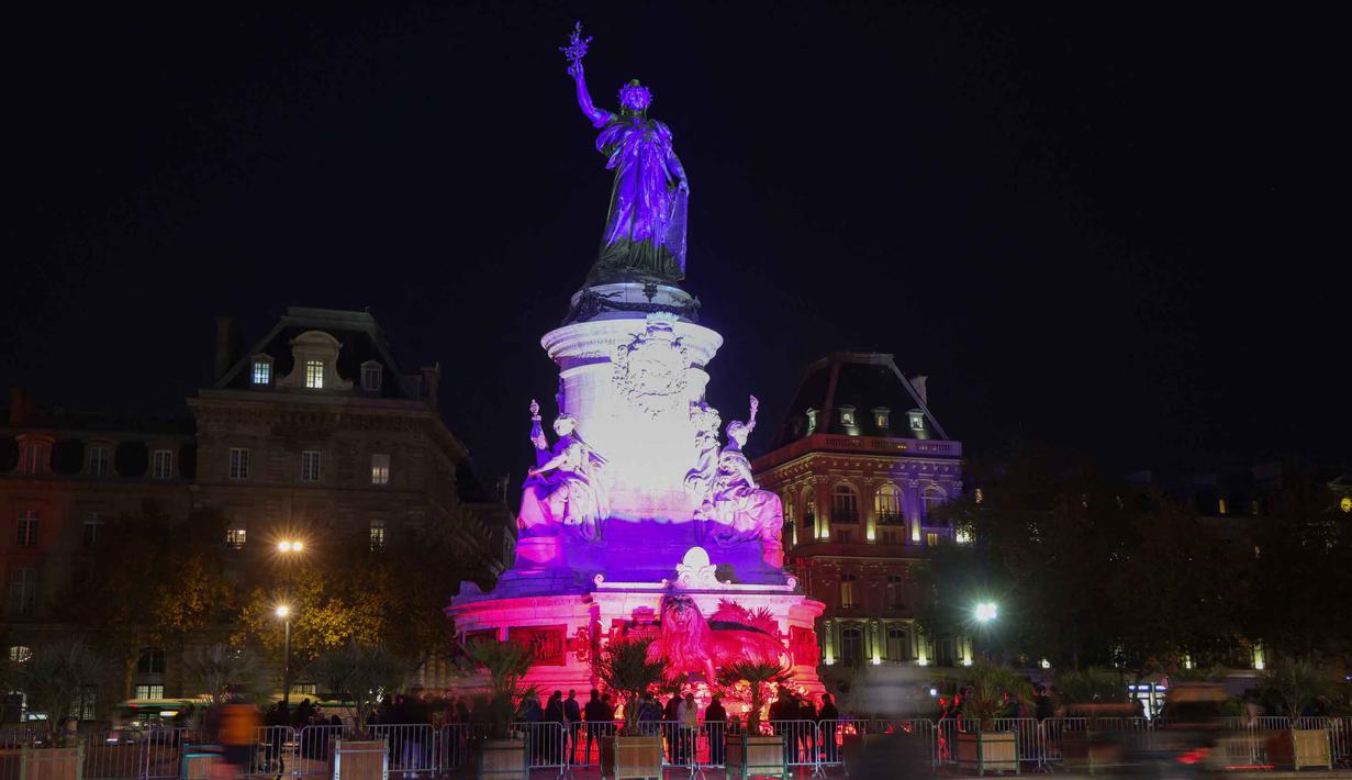 Warga Paris juga berkumpul di Place de la République, di mana upacara penghormatan utama disiarkan secara langsung di layar raksasa. Tampak sebuah foto memperlihatkan Place de la Republique diterangi dengan warna bendera nasional Prancis sebagai penghormatan kepada korban serangan teroris Paris 2015, di Paris, pada 12 November 2025. (Ludovic MARIN/AFP)