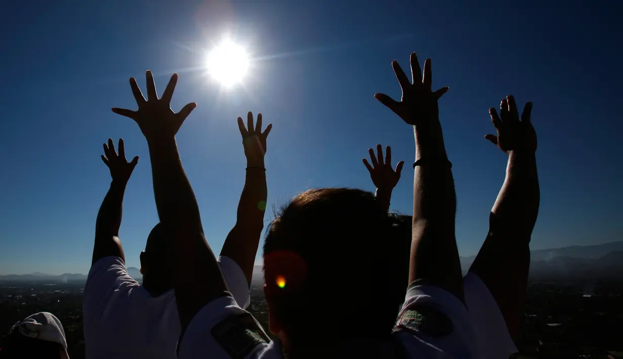 Pengunjung mengangkat tangan mereka untuk menerima energi matahari saat merayakan equinox musim semi di situs arkeologi Teotihuacan, Meksiko (21/3). (AP Photo/Rebecca Blackwell)