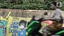 Pengendara motor melintasi mural bertema imbauan protokol kesehatan COVID-19 di kawasan Cakung Barat, Jakarta, Minggu (18/10/2020). Mural karya warga setempat tersebut bertujuan mengingatkan masyarakat akan pentingnya memakai masker, menjaga jarak, dan mencuci tangan. (merdeka.com/Iqbal S. Nugroho)