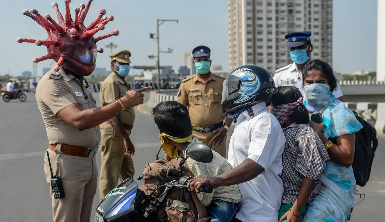 Inspektur polisi Rajesh Babu mengenakan helm berbentuk virus corona saat mengimbau pengendara motor selama lockdown di pos pemeriksaan di Chennai, India, Sabtu (28/3/2020). Cara ini bertujuan agar warga menerapkan social distancing dan tetap berada di rumah selama pandemi Covid-19. (Arun SANKAR/AFP)