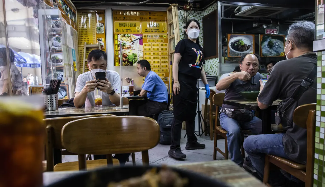 Pelanggan bersantap di sebuah restoran saat pemerintah mengumumkan pelonggaran pembatasan Covid-19 paling ketat, di Hong Kong, Kamis (14/4/2022). Pelonggaran tersebut akan memungkinkan salon kecantikan, bioskop, dan pusat kebugaran dibuka kembali mulai 21 April 2022 mendatang. (ISAAC LAWRENCE/AFP)