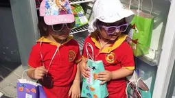 Dua orang anak berfoto di depan kulkas sambil memegang bungkus yang berisi makanan dan minuman jelang bulan Ramadan di Dubai. Kulkas ini disediakan untuk pekerja dan buruh yang akan berbuka puasa di bulan Ramadan. (www.instagram.com/ramadanfridgesdxb)