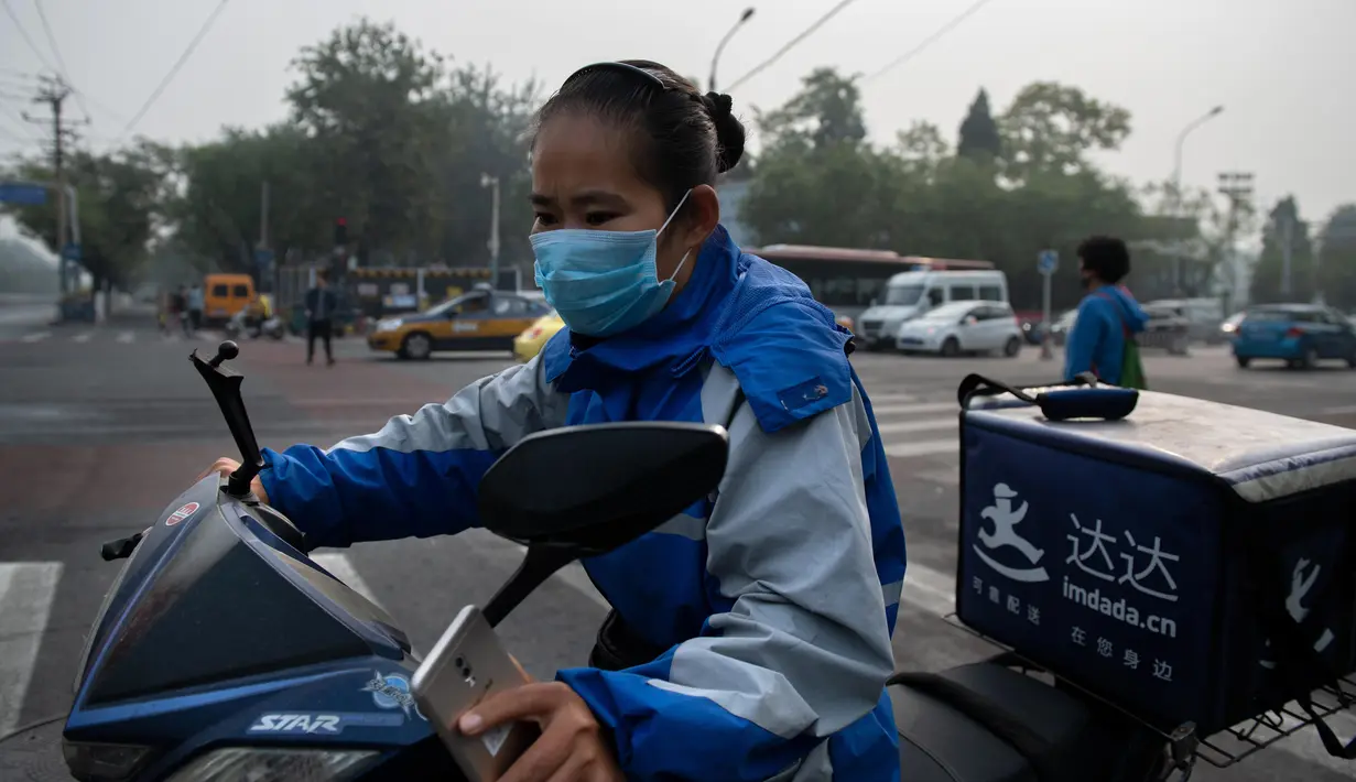 Seorang pekerja pengiriman mengenakan masker pelindung untuk menghindari polusi udara buruk di Beijing (22/10). (AFP Photo/Nicolas Asfaouri)