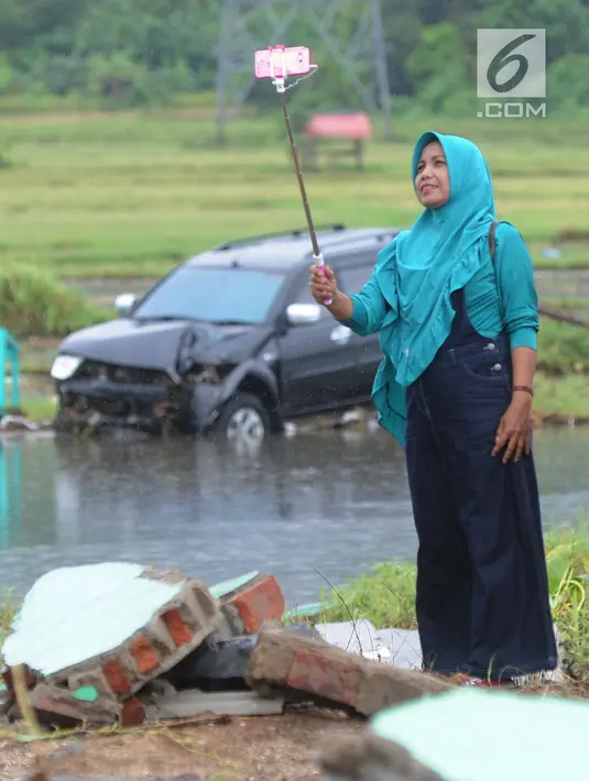 Warga berselfie dengan latar belakang kawasan terdampak bencana tsunami di Carita, Banten, Selasa (25/12). Libur Natal dimanfaatkan warga luar Anyer dan carita untuk menyaksikan langsung terdampak bencana sambil berselfie. (Merdeka.com/Arie Basuki)