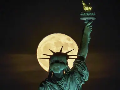Bulan purnama muncul di depan Patung Liberty, New York, Amerika Serikat, 14 Juni 2022. Fenomena ini disebut juga sebagai Strawberry Supermoon karena terjadi pada saat panen strawberry. (AP Photo/J. David Ake)