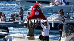 Para penonton memegang maskot Olimpiade Paris 2024 "Phryge" dalam parade kapal di dekat pantai Marseille, di Laut Mediterania, pada tanggal 8 Mei 2024. (NICOLAS TUCAT/AFP)
