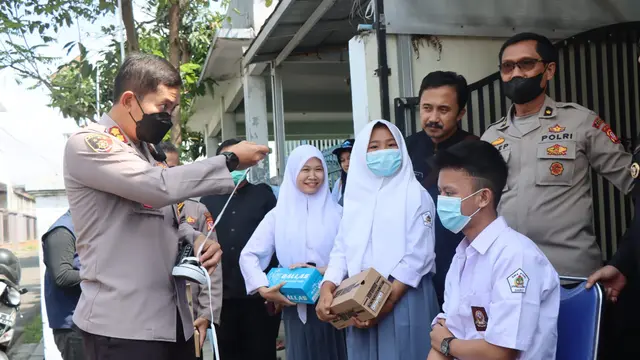 Kapolres Garut AKBP Wirdhanto Hadicaksono membetulkan tali sepatu milik pelajar disela-sela pemberian sepatu korban banjir bandang Garut di kantor desa Jayaraga. (Liputan6.com/ Jayadi Supriadin)