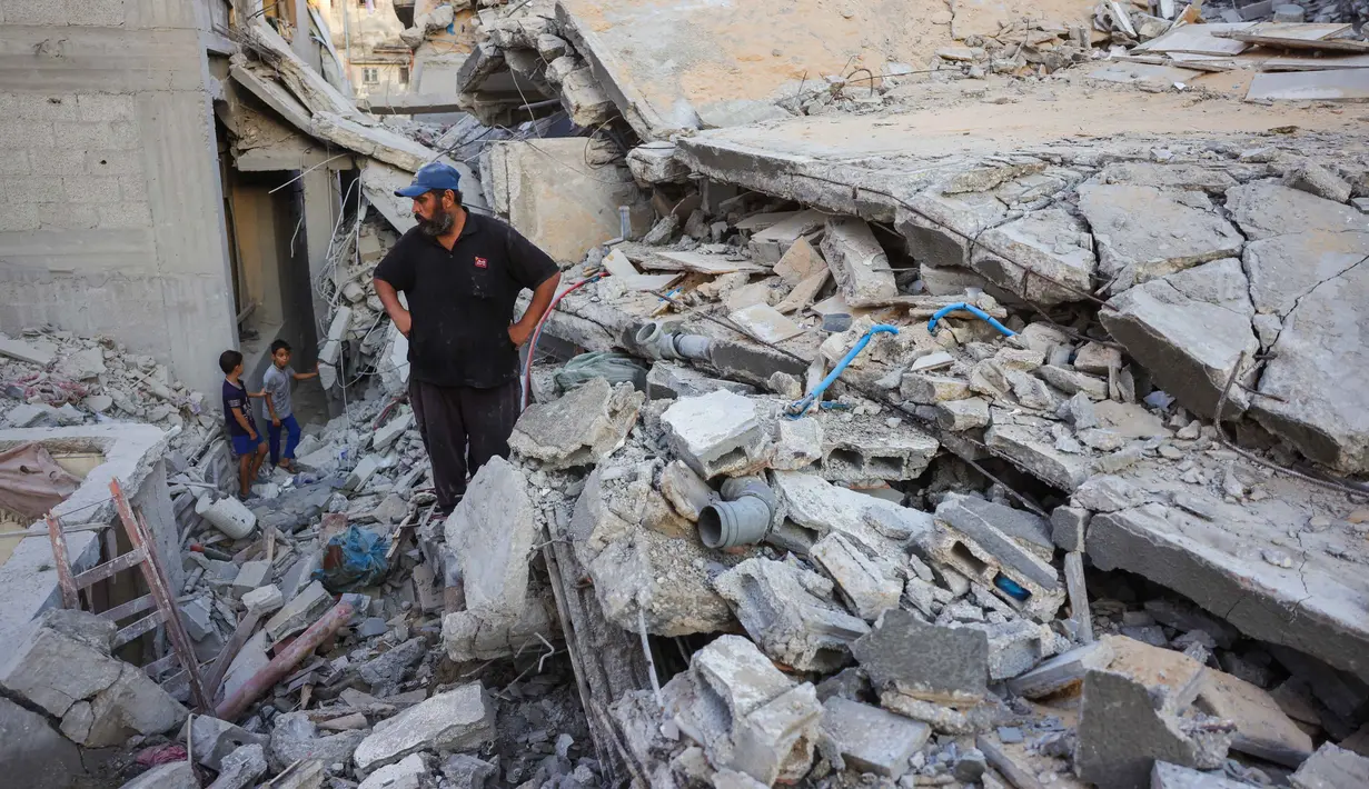 Seorang pria dan anak-anak melihat reruntuhan rumah yang hancur akibat serangan Israel di Khan Younis, Jalur Gaza selatan, pada Rabu 29 Oktober 2025. Untuk diketahui, Israel mulai melancarkan serangan udara sejak 28 Oktober 2025 setelah menuduh Hamas menyerang pasukan Israel di Gaza dan melanggar gencatan senjata. (BASHAR TALEB/AFP)