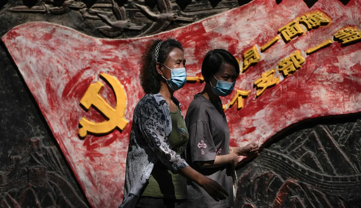 Wanita mengenakan masker wajah berjalan di dekat mural yang menggambarkan bendera partai komunis dan slogan partai di Beijing, Selasa (6/9/2022). China melarang warganya lakukan perjalanan domestik selama liburan nasional mendatang. (AP Photo/Andy Wong)